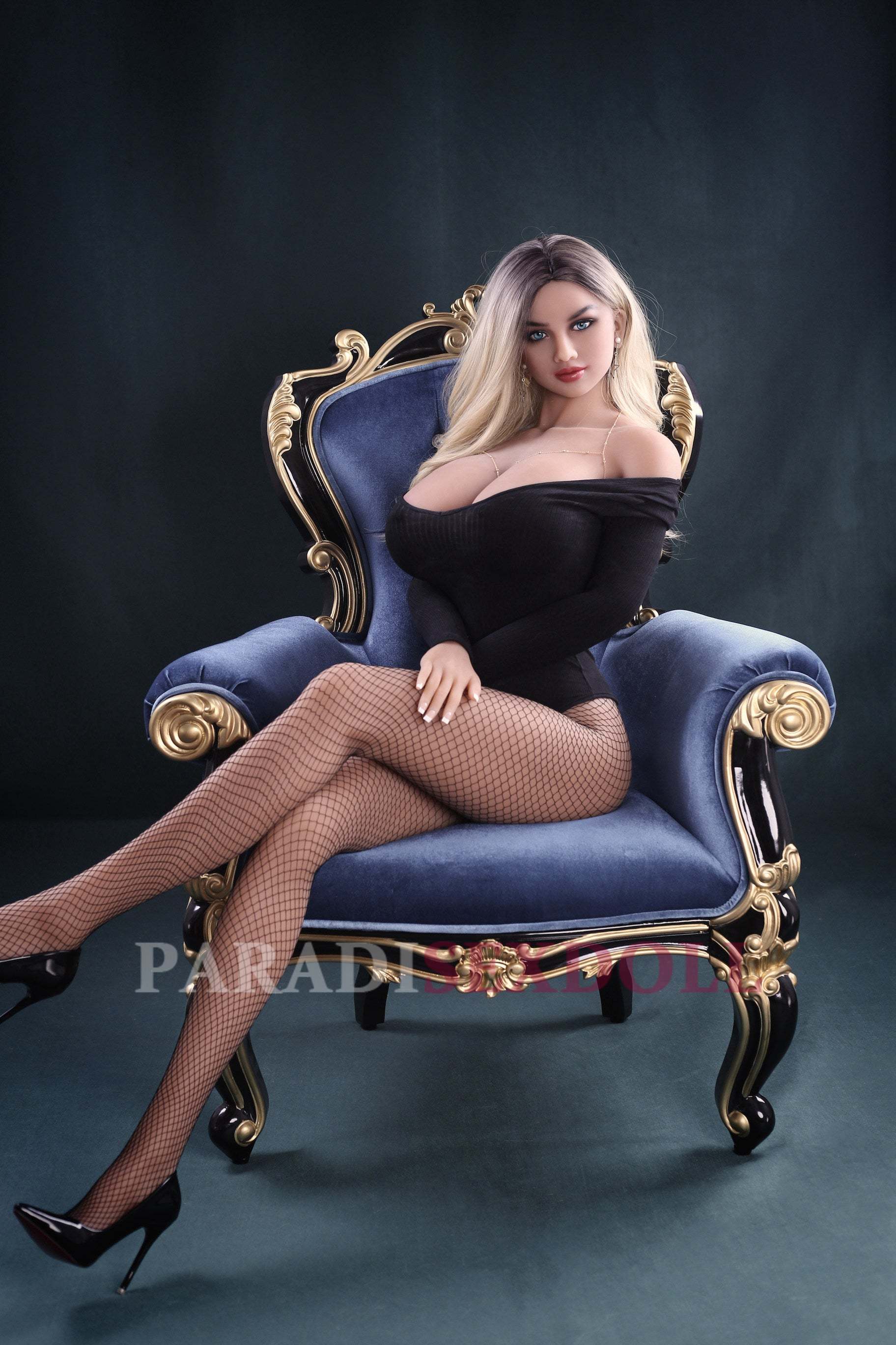 Full-body TPE sex doll Aaliyah posed regally in a lavish blue chair, wearing a stylish black off-shoulder bodysuit and fishnet stockings. Her long blonde hair cascades elegantly, accentuating her lifelike blue eyes and realistic features.