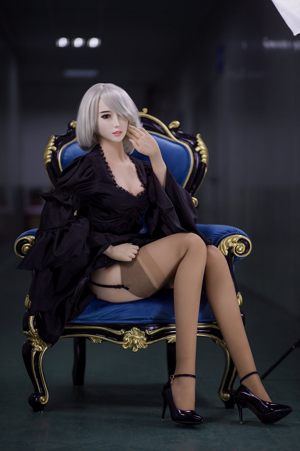 Akiko 170cm realistic sex doll seated elegantly on a royal blue armchair, wearing a black lace robe and sheer stockings, showcasing her sophisticated look with short platinum blonde hair and striking pose.