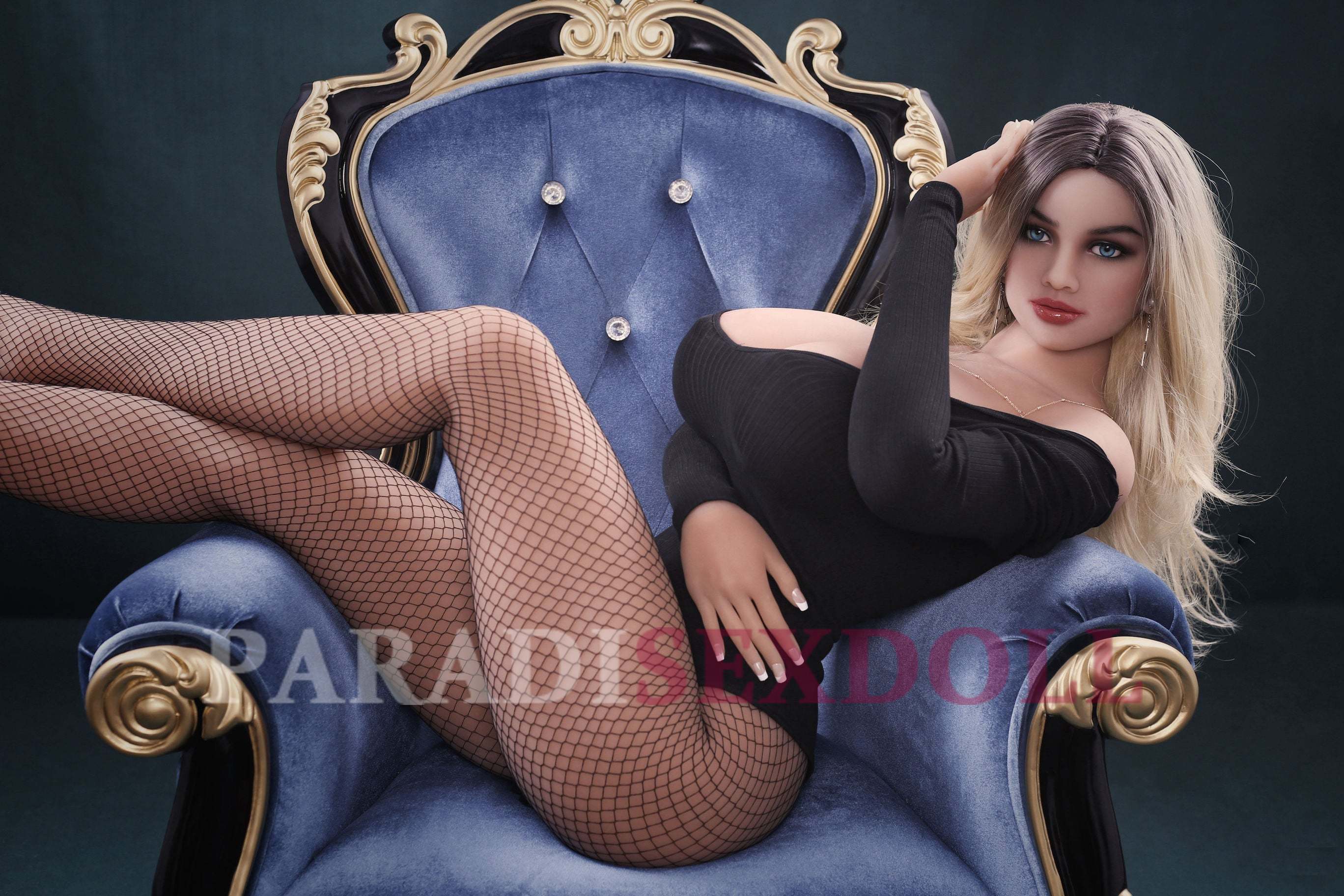 Aaliyah, a lifelike full-body TPE sex doll, reclining elegantly in a plush blue chair. She wears a stylish black off-shoulder bodysuit and fishnet stockings, showcasing her long blonde hair and realistic features, with her hand gracefully positioned on her thigh.