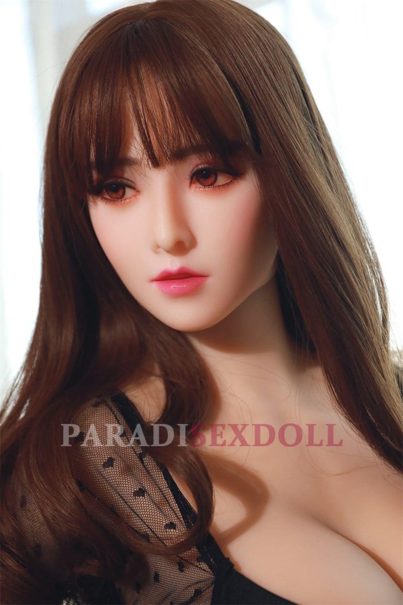 Realistic Korean life-size sex doll Natalie with long brown hair and detailed facial features, wearing a black sheer top, highlighting her ample bust in a bright, well-lit environment with soft natural light.