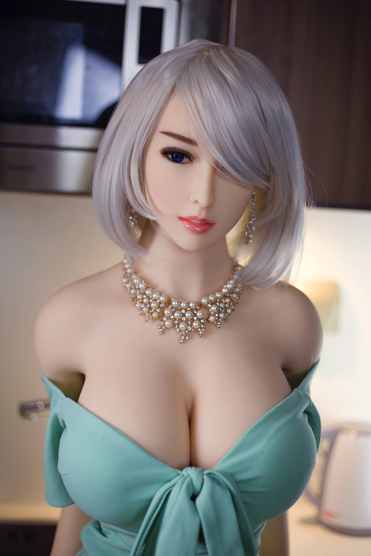 Akiko 170cm realistic sex doll in a light green off-shoulder dress with a pearl necklace, displaying K-Cup breasts and chic blonde hairstyle in a modern kitchen setting.