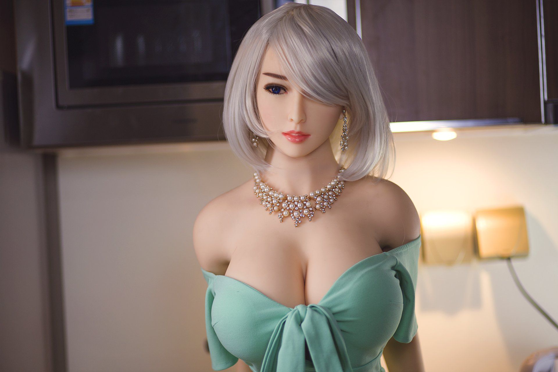 170cm Akiko realistic sex doll featuring K-Cup breasts in a fitted light green off-shoulder dress with a bow, adorned with a pearl necklace, posing elegantly in a contemporary kitchen with soft lighting.