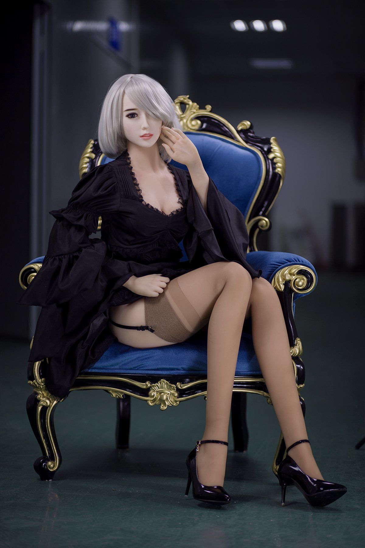 170cm Akiko realistic sex doll seated on an ornate royal blue armchair wearing a black lace robe and sheer stockings, with short platinum blonde hair and high heels, creating an elegant and alluring pose.