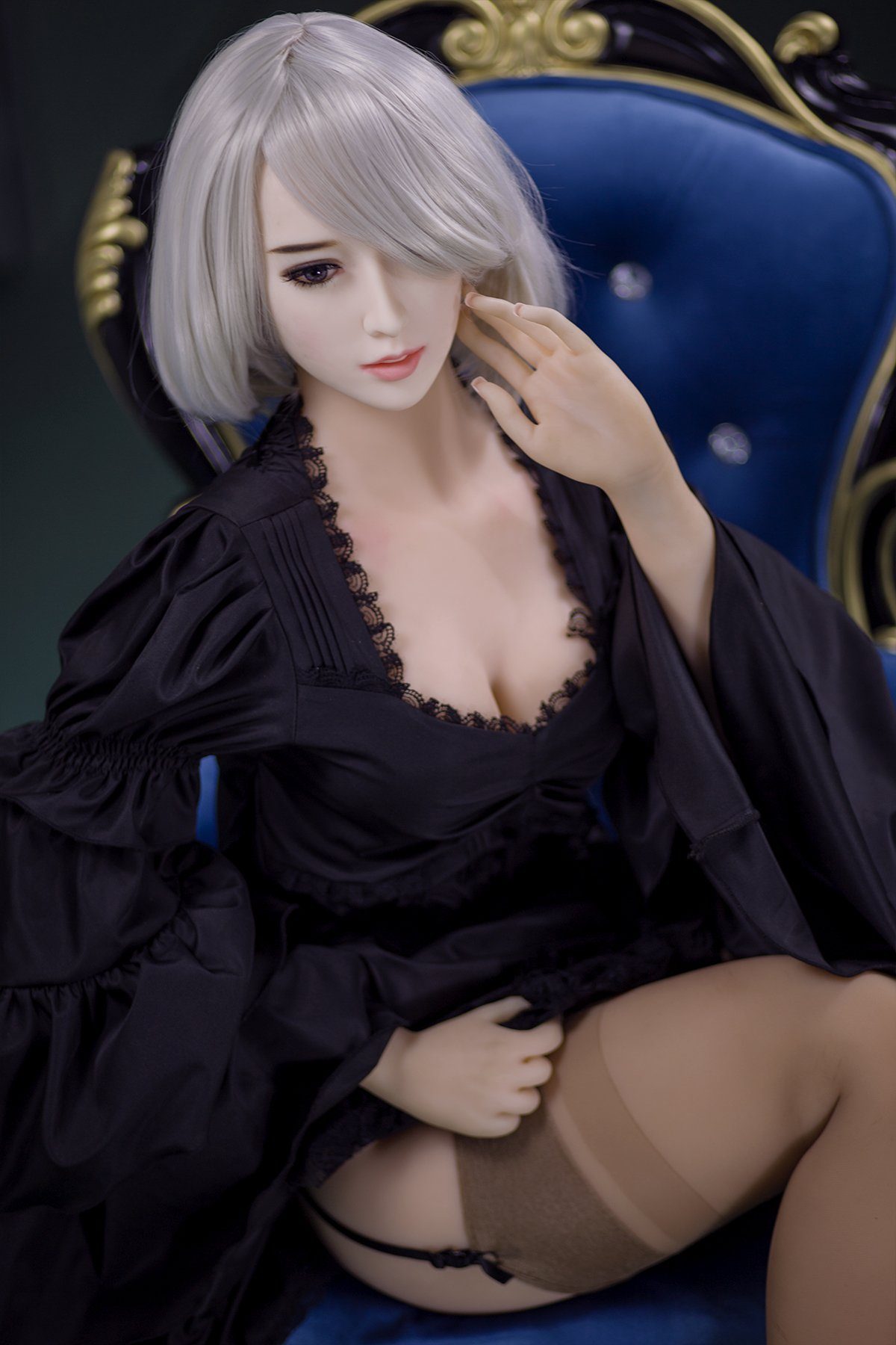 170cm Akiko realistic sex doll wearing an elegant black lace robe with billowy sleeves, showcasing her K-Cup breasts and stylish short platinum blonde hair while seated on a luxurious royal blue armchair.