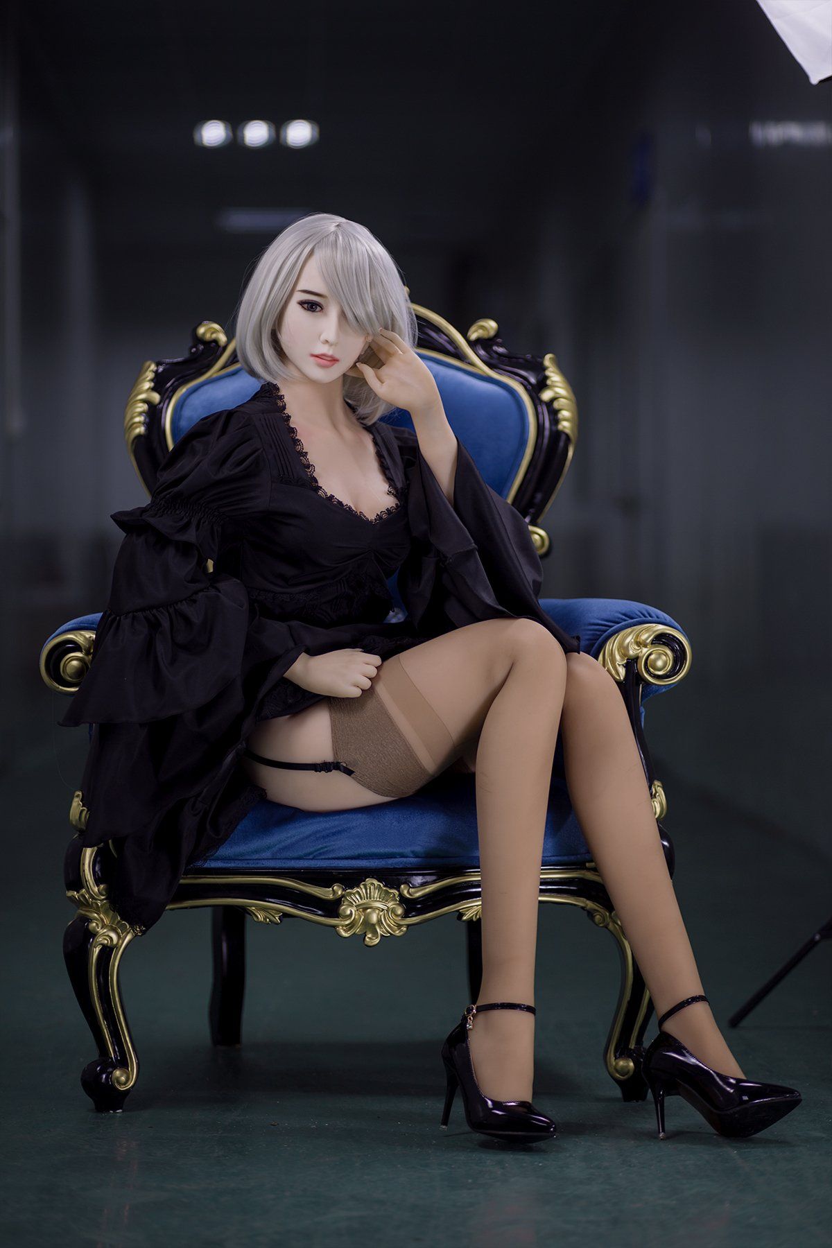 Elegant 170cm Akiko sex doll in a black lace robe with billowy sleeves, showcasing K-Cup breasts and wearing beige stockings, seated gracefully on a royal blue armchair with short platinum blonde hair.