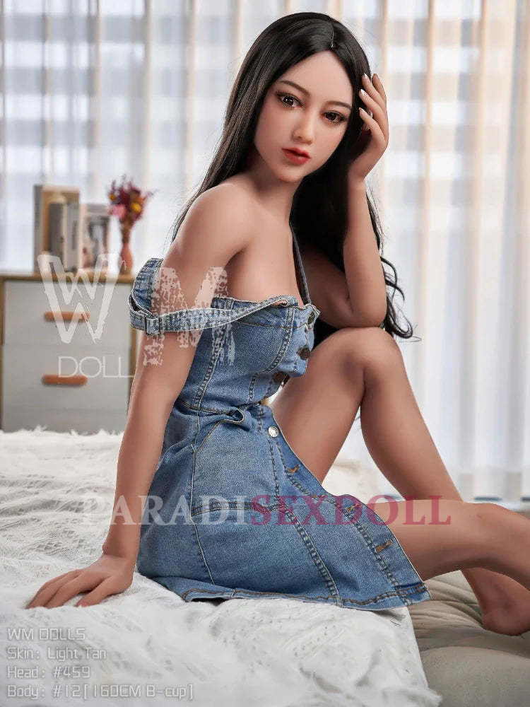 Lifelike Asian TPE sex doll with long black hair, wearing a stylish off-shoulder denim dress, seated gracefully on a sofa in soft natural light, emphasizing her realistic facial features and natural skin texture.