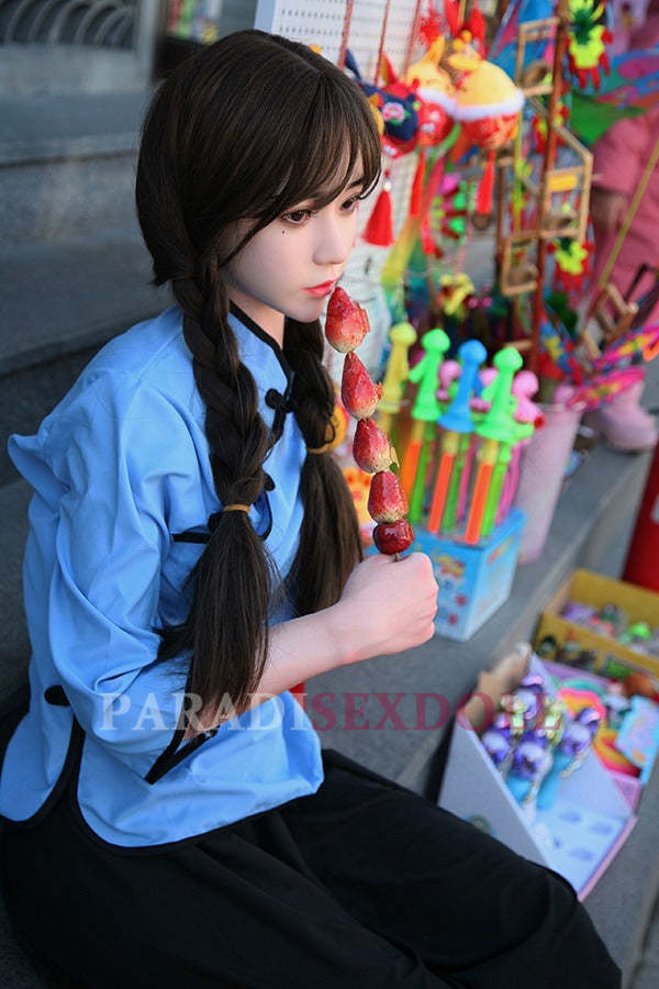 Asian silicone sex doll with long braided hair wearing a blue traditional Chinese top and black pants, seated on steps and holding a colorful fruit skewer, surrounded by vibrant traditional Chinese toys.