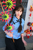 Asian silicone sex doll with long braided hair wearing a blue traditional Chinese top and black pants, holding colorful wheels on a stick, posed against a decorative backdrop.