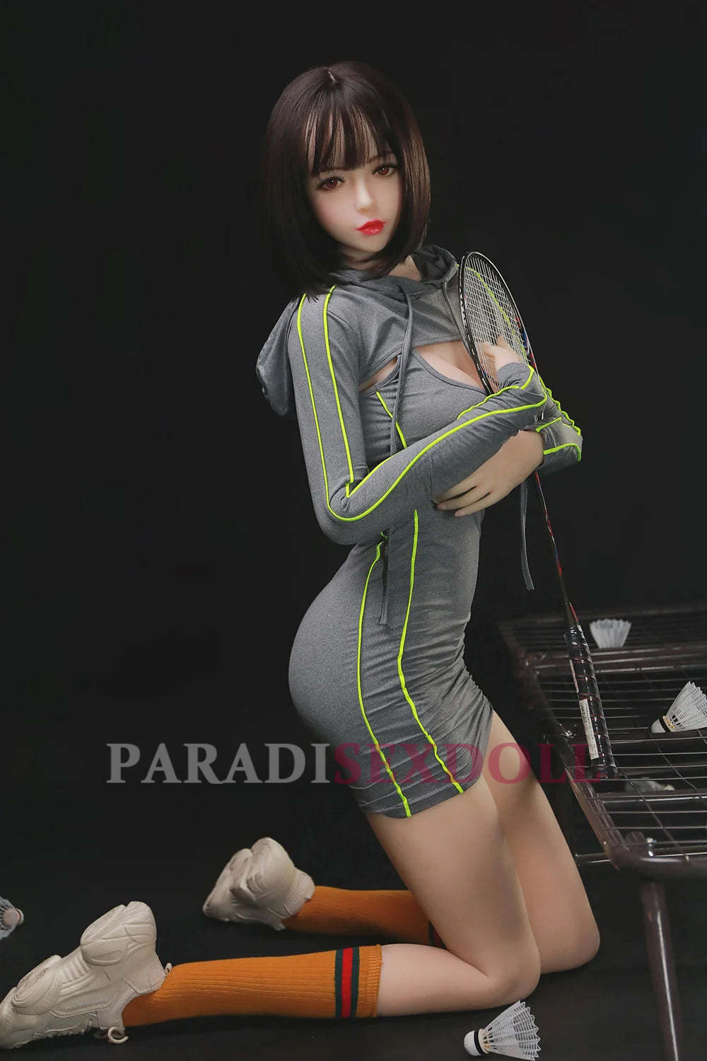 Kneeling 168cm exotic sex doll Olivia in a stylish grey and neon athletic outfit, holding a badminton racket on a court, highlighting her alluring figure and sporty elegance.