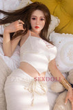 Asian lifelike full silicone sex doll Charlene wearing a stylish two-piece outfit, relaxing on a bed surrounded by plush pillows and a teddy bear, highlighting realistic facial details and long hair.