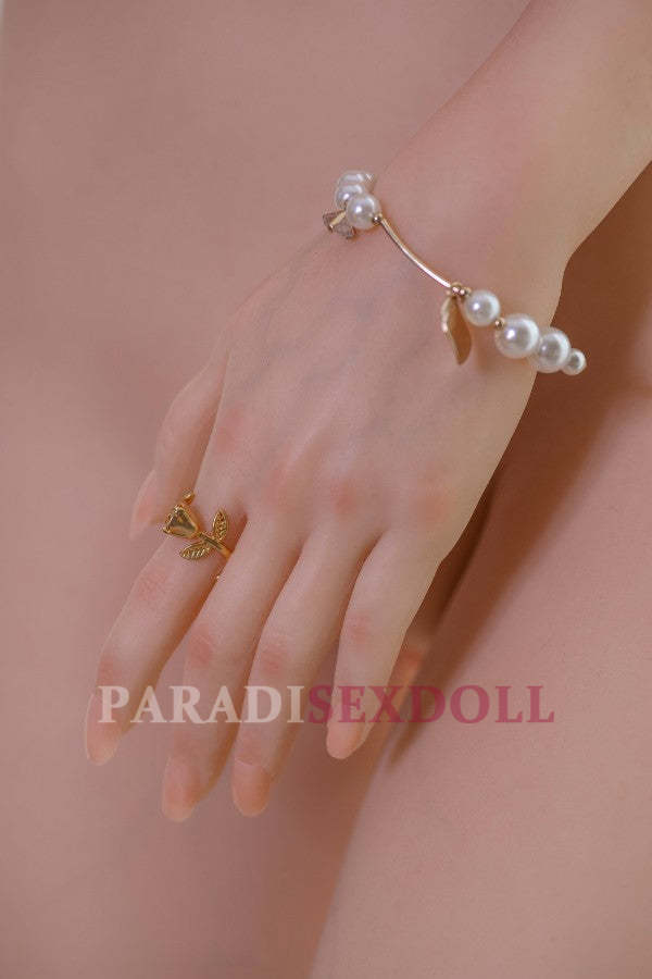 Close-up of the realistic hand of the Asian silicone sex doll Qiuyue, showcasing intricate details of the fingers and a delicate gold ring with a leaf design. The hand is adorned with a pearl bracelet, emphasizing the lifelike quality of the doll.