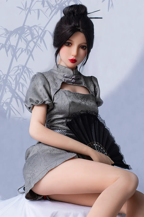 Elegant lifesize Chinese sex doll Winni features small breasts, wearing a chic silver dress with puff sleeves, posed gracefully while holding a black fan, against a soft bamboo-patterned backdrop.