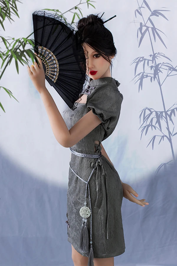 Chinese lifesize sex doll Winni showcasing elegance in a contemporary gray puff-sleeve dress, gracefully holding a black fan, posed against a serene bamboo-patterned backdrop.