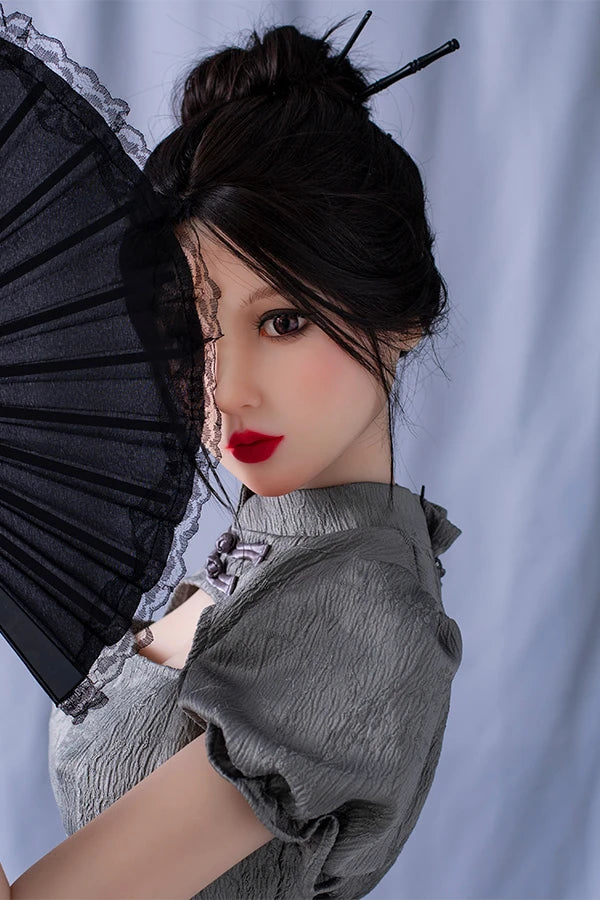 Lifesize Chinese sex doll Winni gracefully holding a black fan in front of her face, wearing a stylish gray puff-sleeve dress, featuring an elegant updo hairstyle with decorative hair sticks, against a soft neutral background.