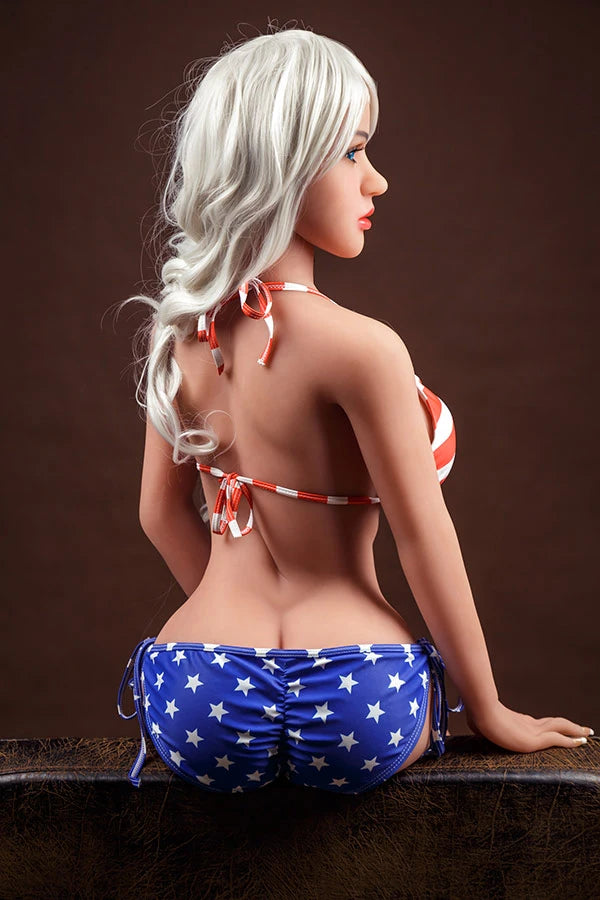 American Beauty love doll Avianna wearing a patriotic bikini with red and white stripes and a blue star-patterned bottom, showcasing her realistic features and long blonde hair from a side angle.