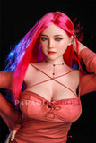 Vibrant pink-haired Rana silicone sex doll wearing a fitted pink top with strap details, showcasing bright blue eyes and realistic features, striking an inviting pose with one hand in her hair against a dark backdrop.