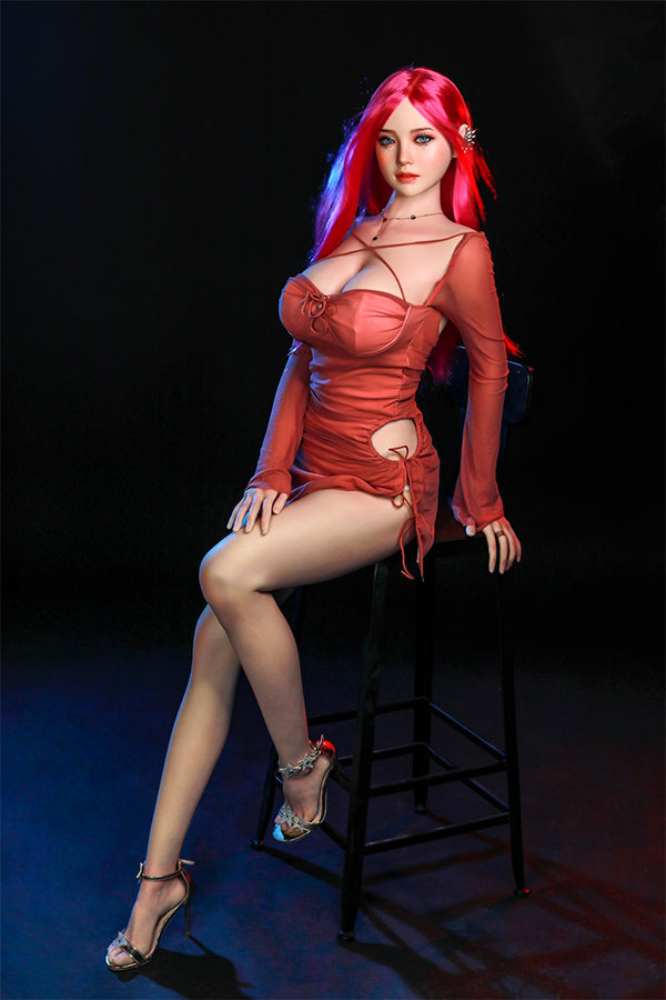 Rana silicone sex doll with long bright pink hair and captivating blue eyes, elegantly seated on a high stool in a fitted coral dress, showcasing her lifelike details and inviting expression in a studio setting.