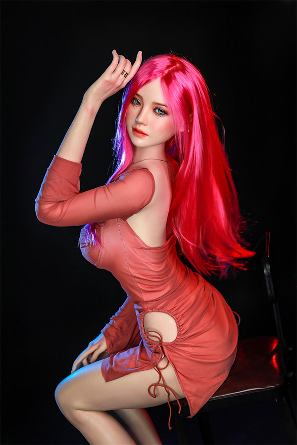 Rana silicone sex doll with long pink hair and captivating blue eyes, striking a playful pose in a fitted coral dress, showcasing her lifelike features and inviting expression.