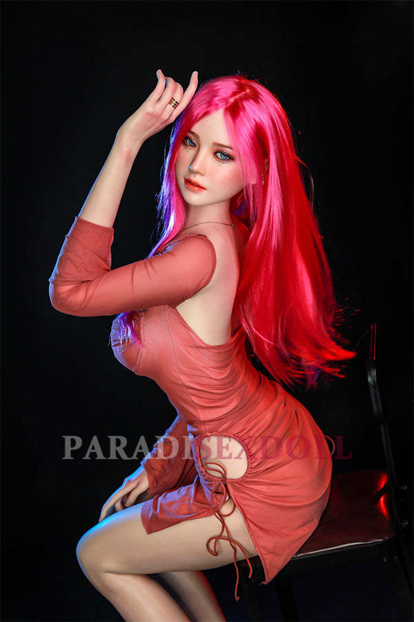 Rana silicone sex doll with long pink hair and captivating blue eyes, striking a playful pose in a fitted coral dress, showcasing her lifelike features and inviting expression.