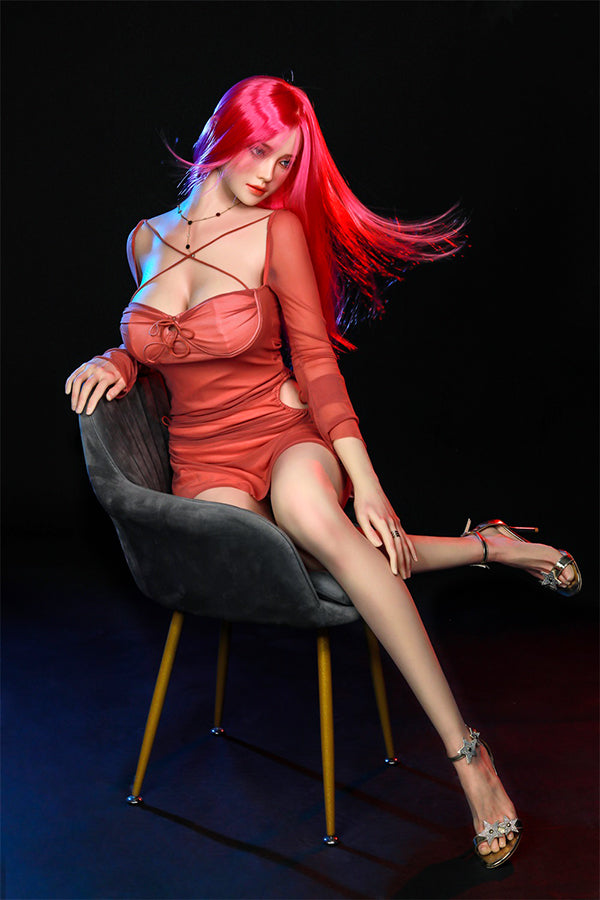 Hyper-realistic Rana silicone sex doll with long bright pink hair and blue eyes, seated gracefully in a stylish chair, wearing a fitted coral dress and showing lifelike features, enhancing her allure and captivating appearance.