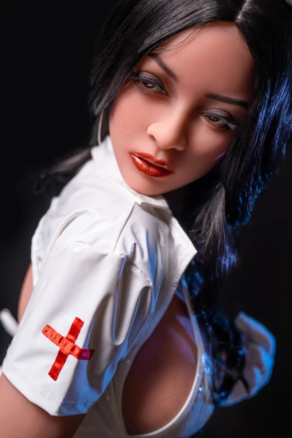 Close-up of Big Booty Black Sex Doll Seraphine in a seductive nurse outfit featuring a tight white costume with a red cross on the sleeve. Her long black hair frames her face, enhancing her lifelike features and sultry expression in a dimly lit setting.